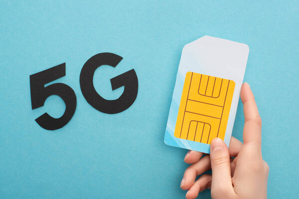 cropped view of woman holding sim card near 5g lettering on blue background