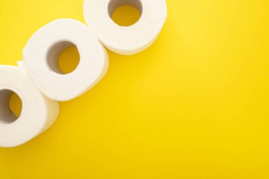 Sarı zemin üzerinde beyaz tuvalet kağıdı rulolarının üst görünümü kopya alanı ile