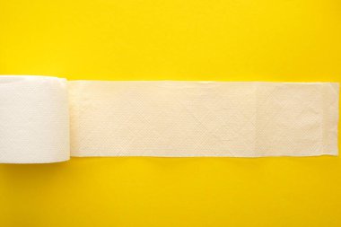 top view of unrolled white toilet paper on yellow background clipart