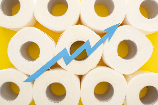top view of blue arrow on white toilet paper rolls on yellow background