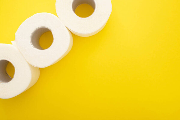 top view of white toilet paper rolls on yellow background with copy space