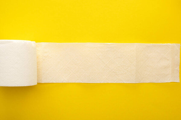 top view of unrolled white toilet paper on yellow background