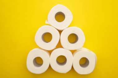 top view of white toilet paper rolls arranged in pyramid on yellow background clipart