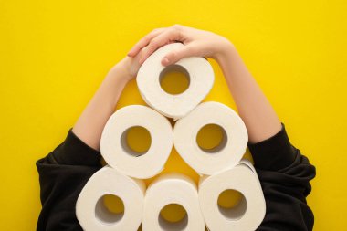cropped view of woman grabbing white toilet paper rolls arranged in pyramid on yellow background clipart