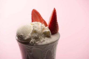Selective focus of milkshake with ice cream and strawberry halves on pink background clipart