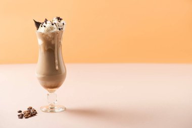 Bej ve portakallı kahve tanelerinin yanında dondurmalı ve çikolatalı bir bardak milkshake.