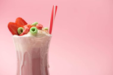 Glass of milkshake with ice cream, colorful candies, strawberry halves and drinking tube on pink background clipart