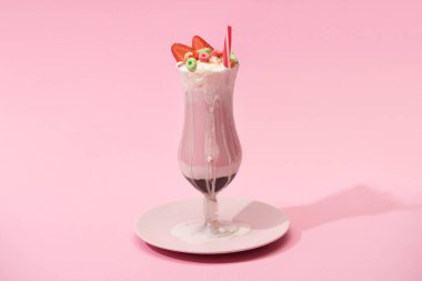 Bir bardak çilekli milkshake, şekerler ve pembe arka planda pipet içmek.