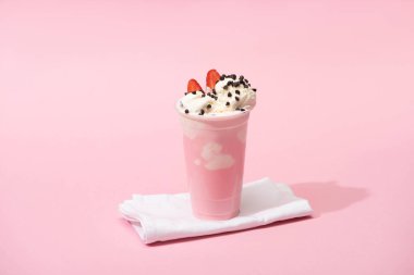 Çikolata parçalı tek kullanımlık milkshake ve pembe arka planda çilekli yarımlar.