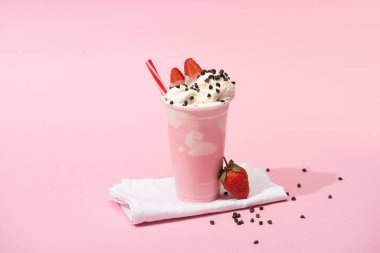 Pembe arka planda saman, çikolata parçacıkları ve çilekli tek kullanımlık milkshake.