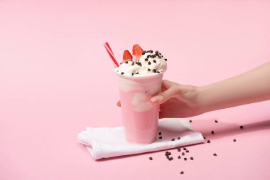 Cropped view of female hand with disposable cup of milkshake with chocolate morsels and strawberry on napkins on pink clipart