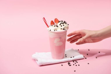 Tek kullanımlık milkshake, çikolata parçalı ve pembe peçeteli çilekli kadın eli kısmen görülüyor.