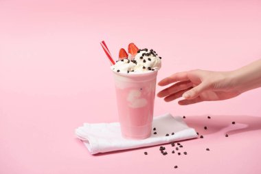 Partial view of female hand with disposable cup of milkshake with chocolate morsels and strawberry on napkins on pink clipart