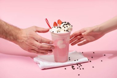 Partial view of female and male hands with disposable cup of strawberry milkshake with chocolate morsels on napkins on pink clipart