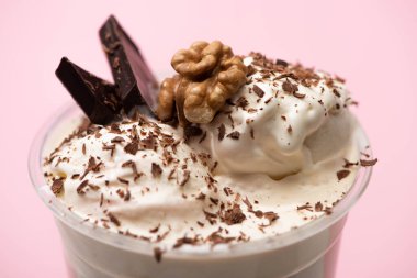 Disposable cup of milkshake with ice cream, walnut, chocolate shavings and pieces on pink background clipart