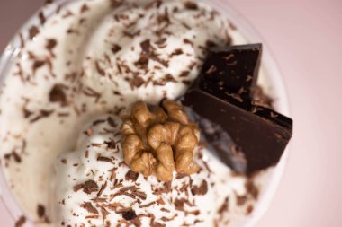 Dondurma, ceviz, çikolata talaşı ve pembe arka planda parçaları olan tek kullanımlık milkshake 'in en iyi görüntüsü.