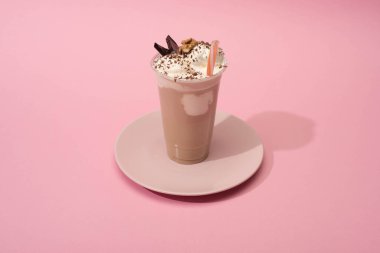 Tek kullanımlık çikolatalı milkshake 'in pembe arka planda saman içerken yüksek açılı görüntüsü.