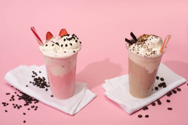 Disposable cups of chocolate and strawberry milkshakes with coffee grains on napkins on pink background clipart