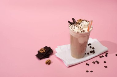 Yüksek açılı tek kullanımlık milkshake fincanı, ceviz, çikolata parçaları ve peçeteli kahve taneleri.