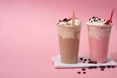 Tek kullanımlık çikolatalar ve çilekli milkshake. Pembe peçetelerde pipet ve kahve taneleri var.