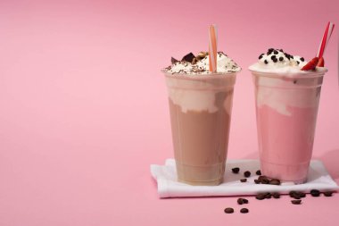 Disposable cups of chocolate and strawberry milkshakes with drinking straws and coffee grains on napkins on pink clipart