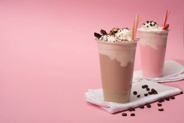 Tek kullanımlık çikolataların ve çilekli milkshake 'lerin seçici odak noktası pembe arka plandaki peçetelerde kahve taneleri.