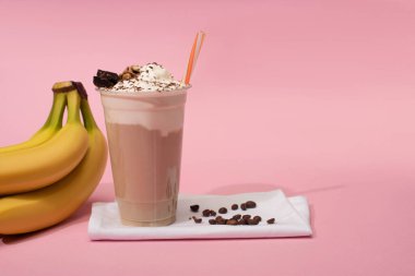 Tek kullanımlık çikolatalı milkshake, peçetelerin üzerinde kahve taneleri, muzların yanında pembe.