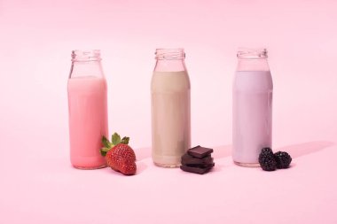 Çilekli milkshake şişeleri, böğürtlen ve pembe arka planda çikolata parçaları.