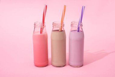 Çilekli, çilekli ve çikolatalı milkshake şişeleri pembe arka planda pipet içiyorlar.