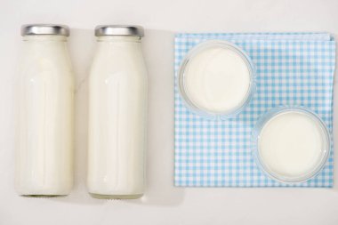 Top view of bottles and glasses of homemade yogurt on plaid cloth on white background clipart