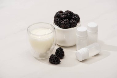 High angle view of sugar bowl with blackberries near glass of homemade yogurt and containers with starter cultures on white  clipart