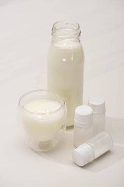 High angle view of bottle and glass of homemade yogurt near containers with starter cultures on white background clipart
