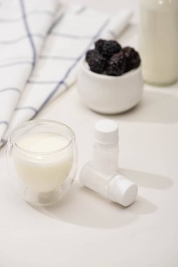 Selective focus of glass of yogurt and containers with starter cultures near fabric and sugar bowl with blackberries on white   clipart