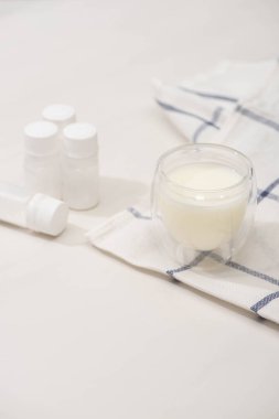 Selective focus of glass of homemade yogurt on cloth near containers with starter cultures on white clipart
