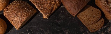 top view of cut whole grain bread on stone black surface, panoramic shot clipart