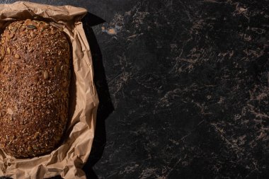 Taze fırınlanmış somun ekmeğin üst görüntüsü taştan siyah bir yüzey üzerinde kağıt üzerinde.