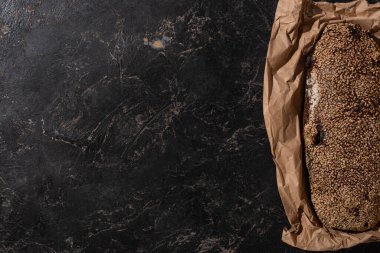 Taze pişmiş somun ekmeğin üst görüntüsü. Taş siyah yüzey üzerinde susamlı kağıt.