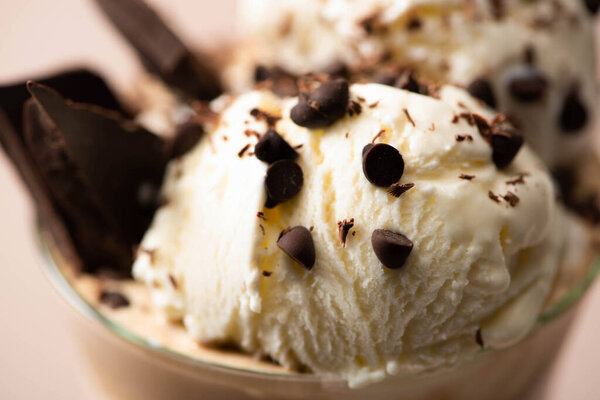 Selective focus of glass of milkshake with ice cream, pieces of chocolate and candies on beige 