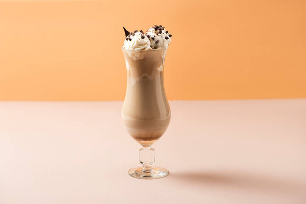 Стакан молочного коктейля с мороженым и шоколадными кусочками на бежевом и оранжевом
