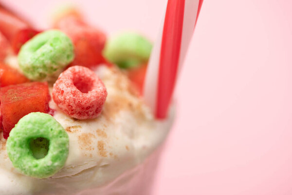 Selective focus of strawberry milkshake with ice cream, colorful candies and drinking tube on pink background