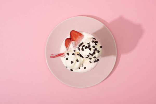 Top view of milkshake with drinking straw and strawberry halves on plate on pink background