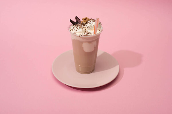 High angle view of disposable cup of chocolate milkshake with drinking straw on plate on pink background