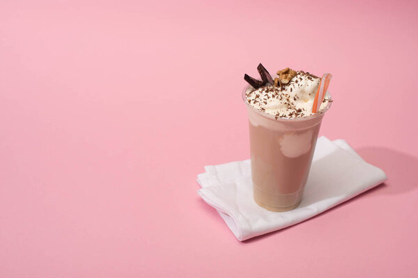 High angle view of disposable cup of chocolate milkshake with drinking straw on napkins on pink background