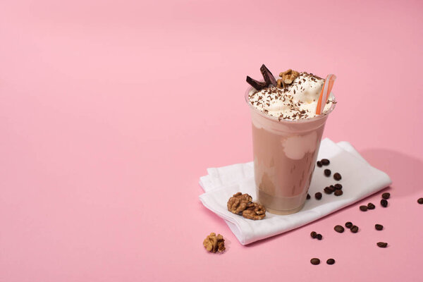 High angle view of disposable cup of chocolate milkshake with walnuts and coffee grains on napkins on pink