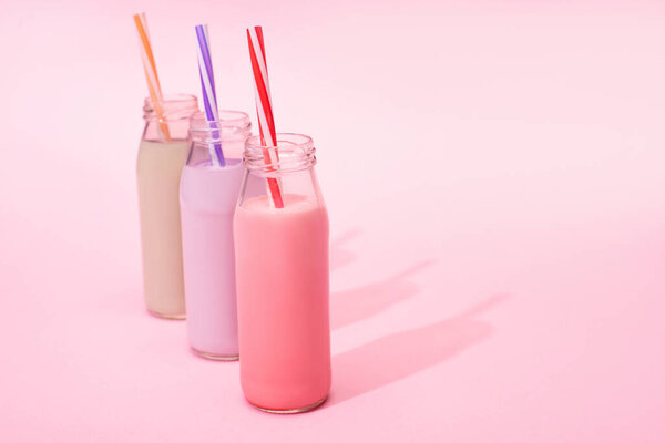 Bottles of colorful berry, strawberry and chocolate milkshakes with drinking straws on pink background