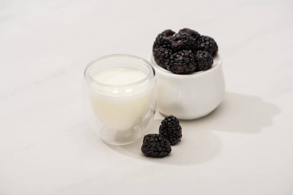 High angle view of sugar bowl with blackberries near glass of homemade yogurt on white background