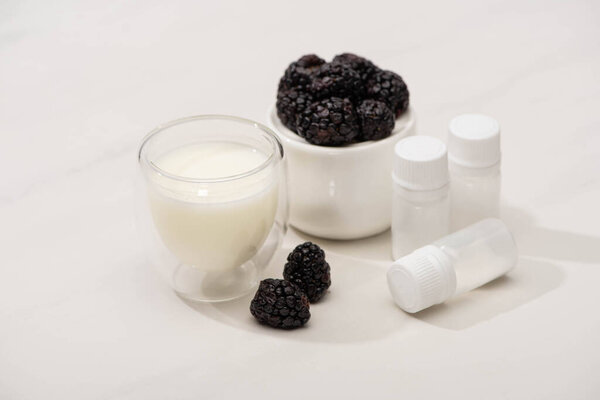 High angle view of sugar bowl with blackberries near glass of homemade yogurt and containers with starter cultures on white 