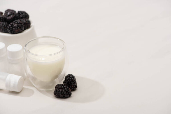 High angle view of blackberries near glass of homemade yogurt and containers with starter cultures on white 