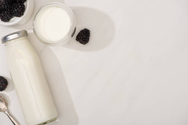Top view of bottle and glass of homemade yogurt with blackberries on white background
