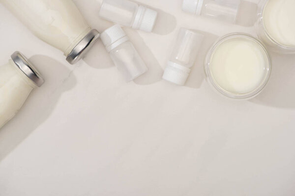 Top view of bottles and glasses of yogurt near containers with starter cultures on white